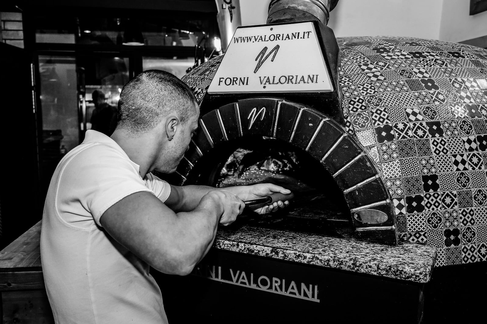 Pizzaiolo al lavoro davanti al forno a legna in una fotografia in bianco e nero